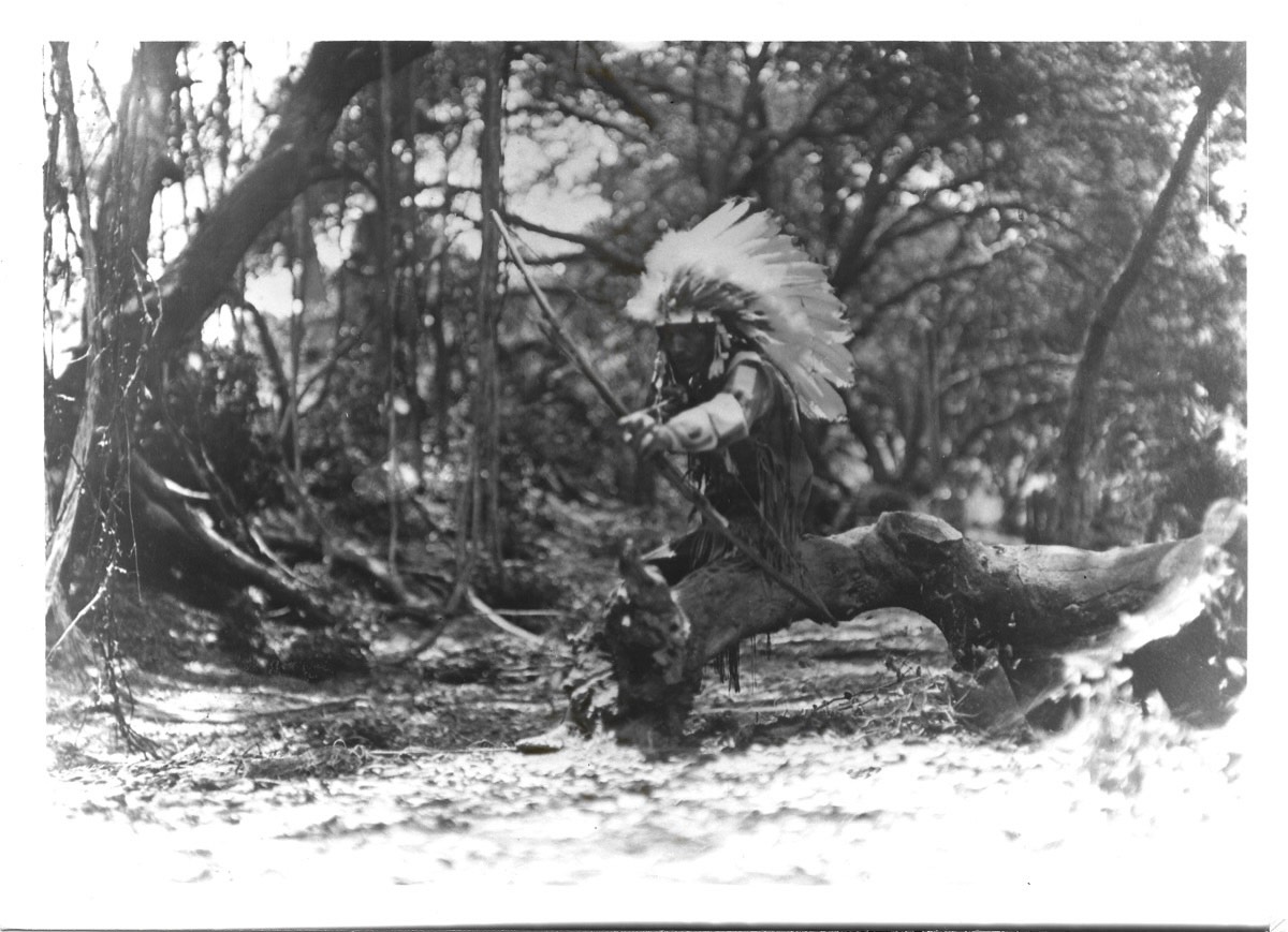 Little Bison shooting a bow in traditional regalia